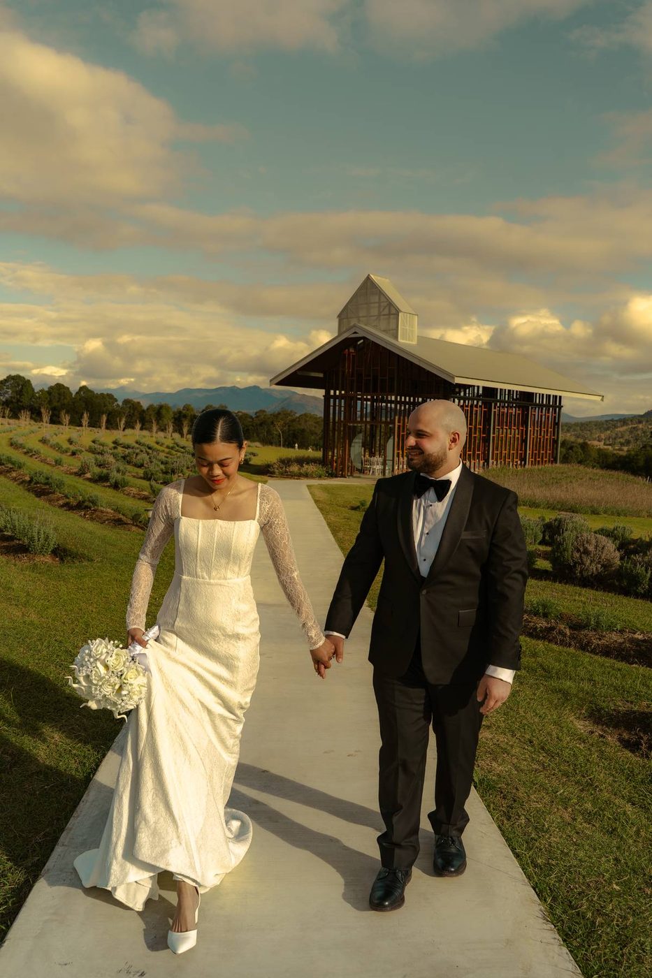 Bride and groom walking the path from the chapel, hand in hand